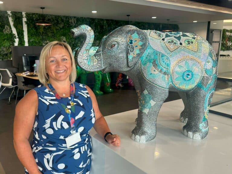 Sarah Nash standing next to a baby elephant sculpture covered in thousands of sparkly rhinestones