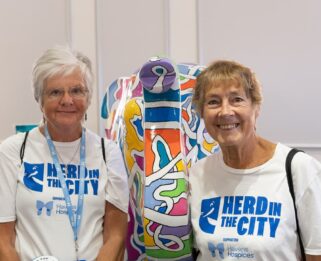 Two volunteers either side of a brightly coloured elephant sculpture, wearing Herd In The City t-shirts