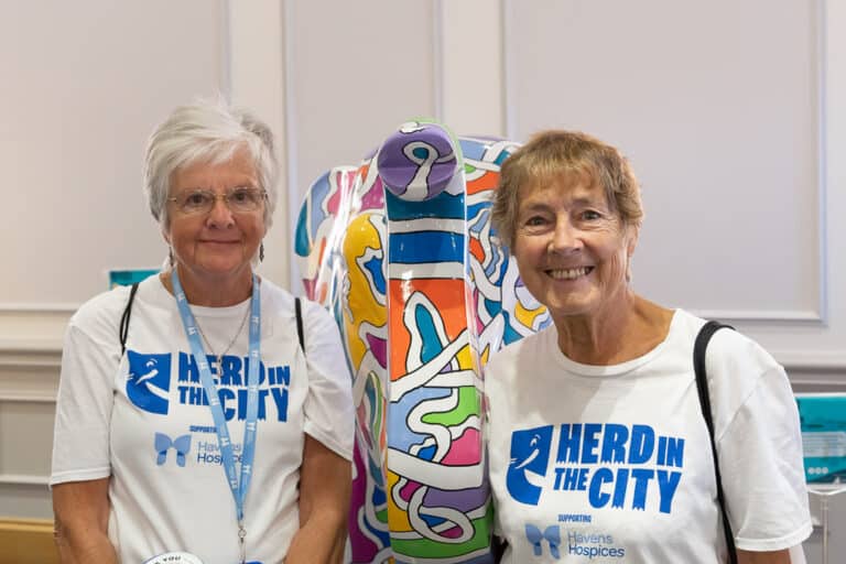Two volunteers either side of a brightly coloured elephant sculpture, wearing Herd In The City t-shirts
