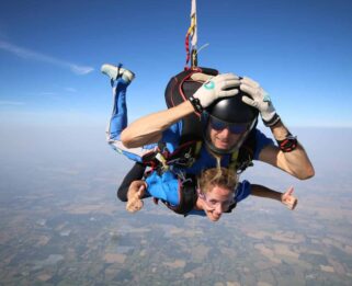 Lisa falling through the sky attached to skydiving instructor. Views of the sky and scenery on the ground.