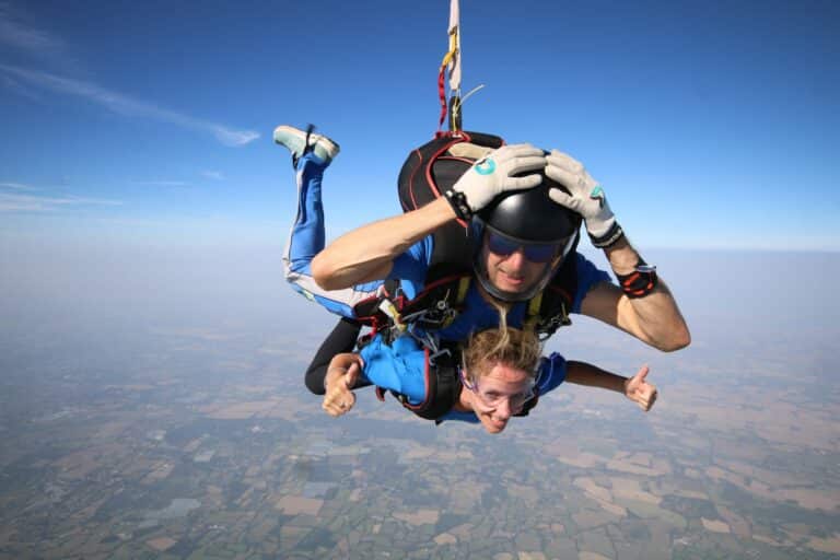 Lisa falling through the sky attached to skydiving instructor. Views of the sky and scenery on the ground.