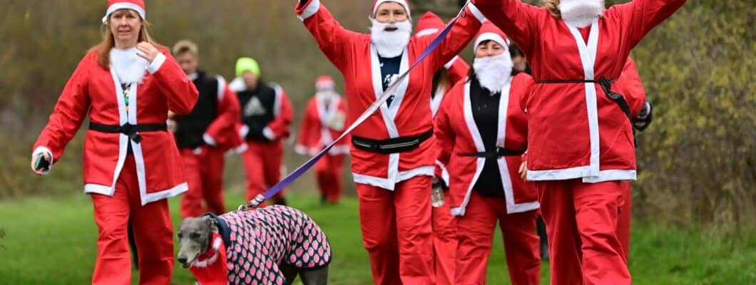 Several people dressed as Santa Claus holding their hands up in Wat Tyler Park, along with a dog on a lead