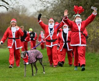 Several people dressed as Santa Claus holding their hands up in Wat Tyler Park, along with a dog on a lead