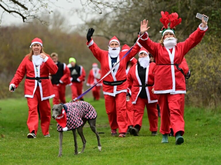 Several people dressed as Santa Claus holding their hands up in Wat Tyler Park, along with a dog on a lead