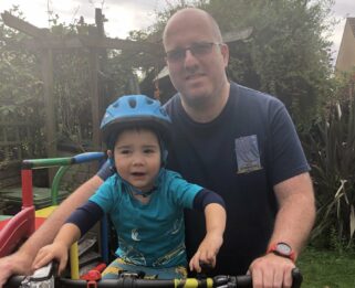 Simon alongside his son Archie who is sitting on his bicycle.