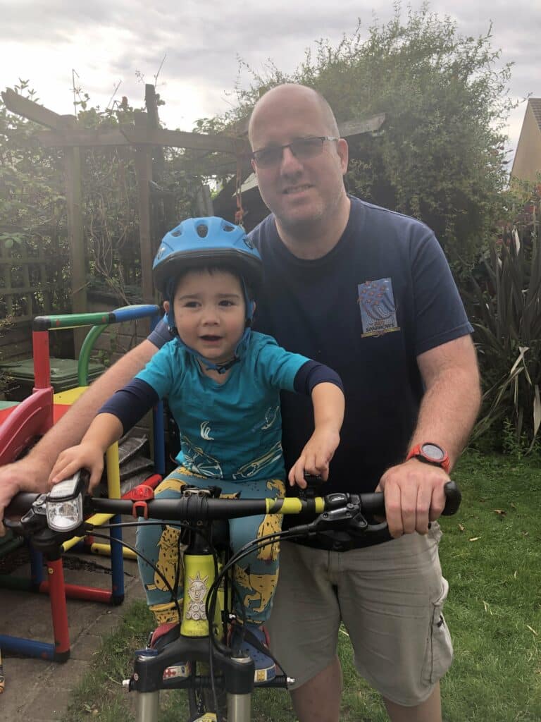 Simon alongside his son Archie who is sitting on his bicycle.