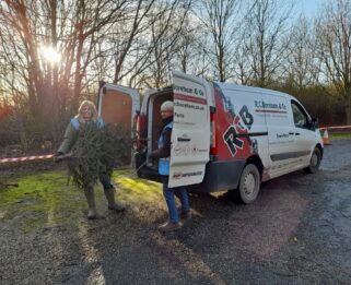 Two supporters standing in a woodland area beside their company van holding a real Christmas Tree