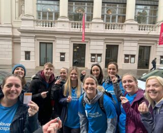 A group of people wearing Havens Hospices t-shirts standing in Bow Street, London holding up a Monopoly board game card labelled Bow Street