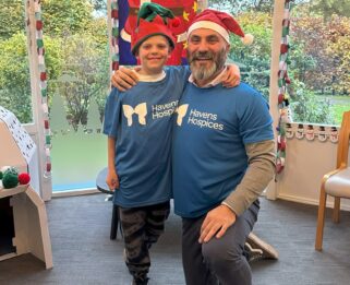 Jack and Rob wearing Havens Hospices t-shirts and elf and Santa hats in front of a festive backdrop