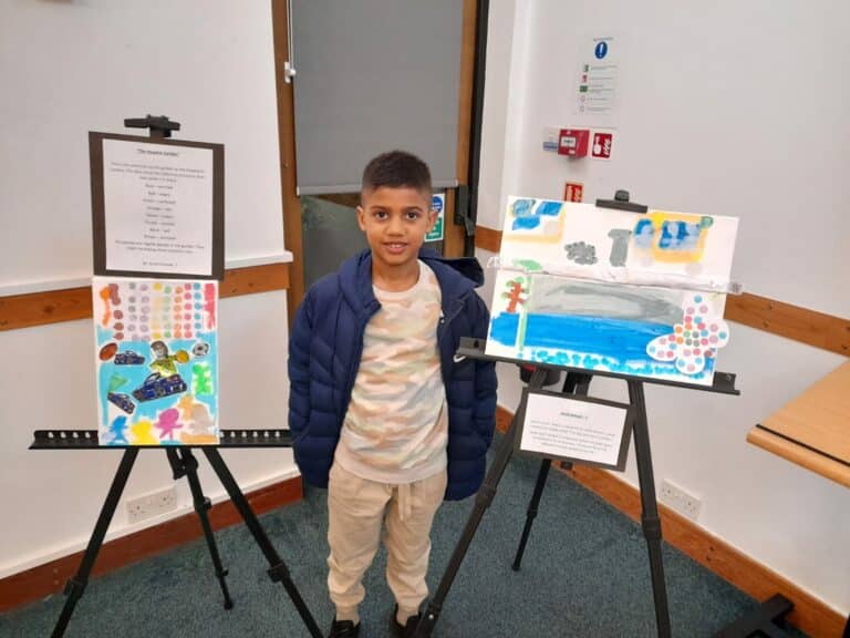 A young boy standing next to his paintings smiling