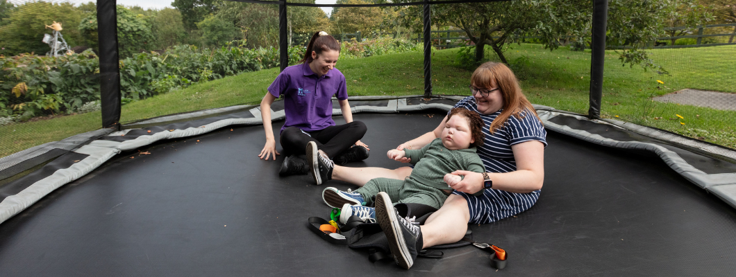 little boy with his mum and a healthcare assistant on the trampoline at Little Havens