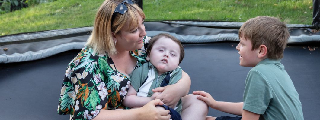 Little boy in his mums arms on trampoline with his brother