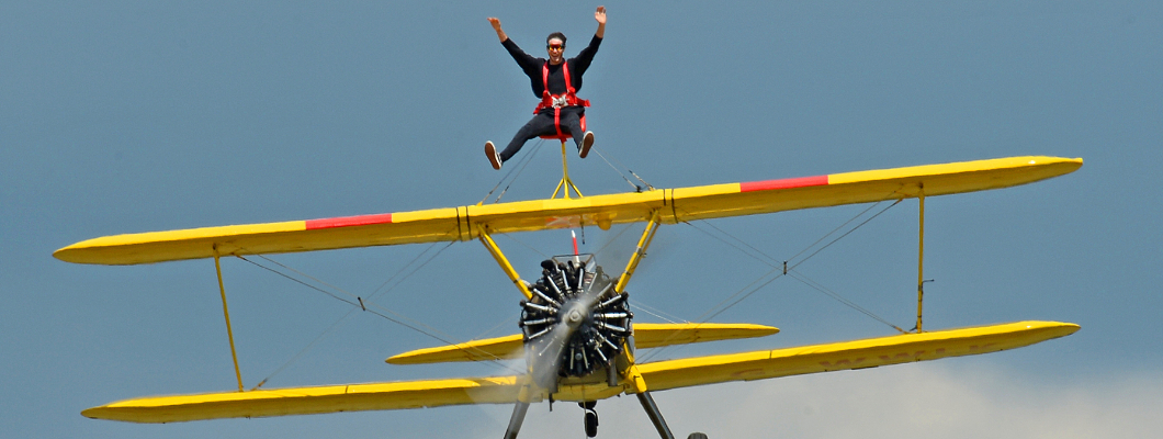 A wing walking participant on top of a flying aeroplane, their arms outstretched.