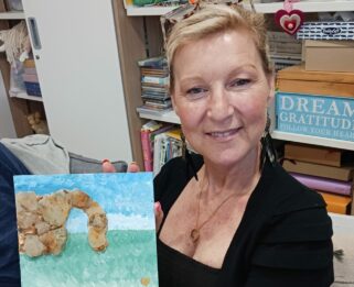 Paula smiling with her sea glass art work in the Fair Havens Hub