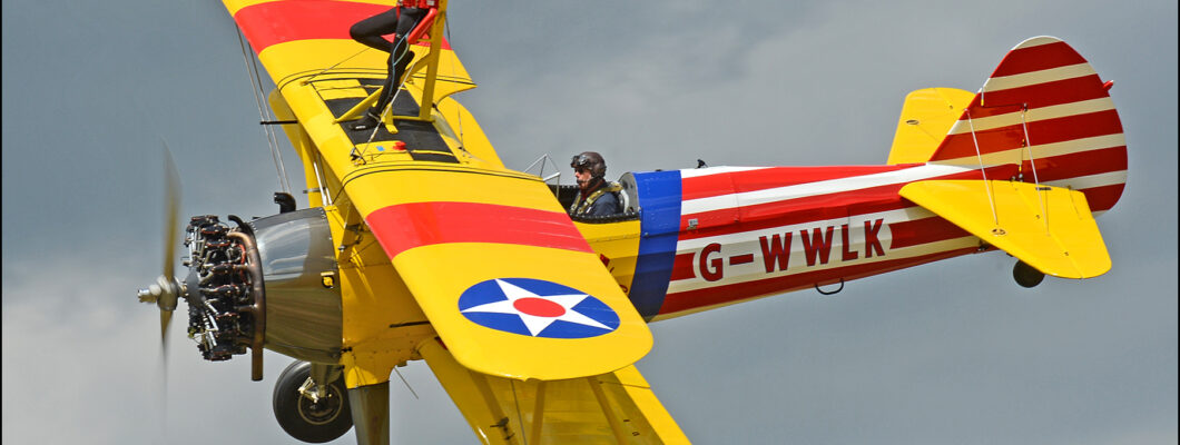 Woman standing on top of a flying aeroplane, her arms are outstretched.