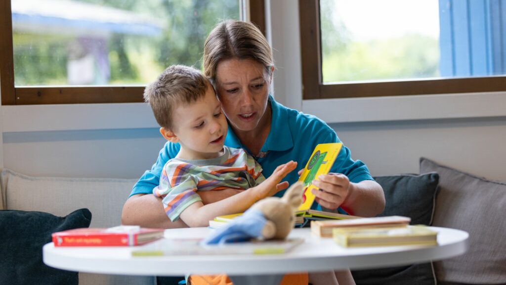 Little boy reading a book with a nurse at Little Havens
