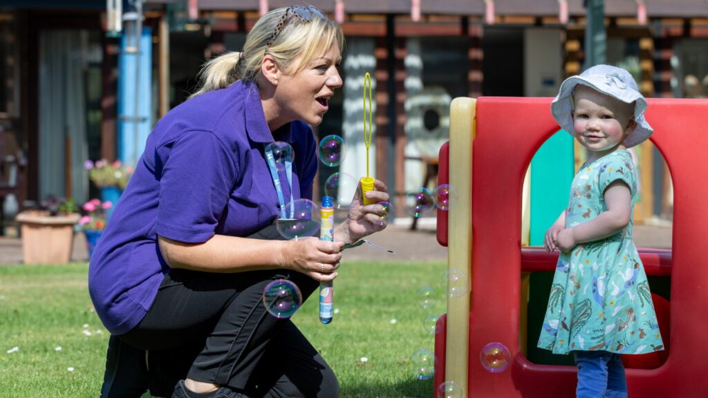 Little girl playing with bubbles with a health care assistant in the Little Havens garden