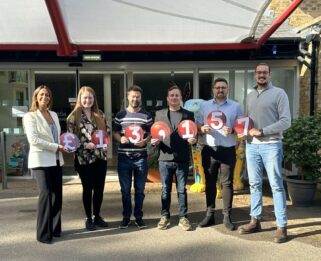 Six people holding cricket ball signs reading £13,157 outside Little Havens Children's Hospice