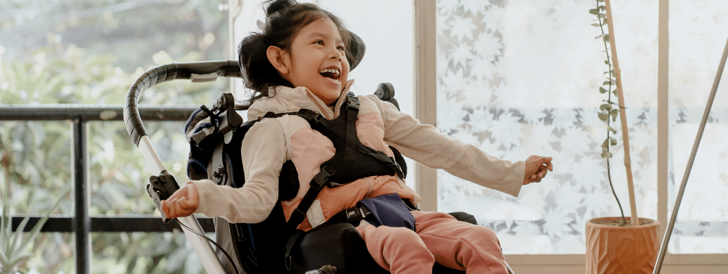 young girl in a wheelchair with a chest strap and smiling
