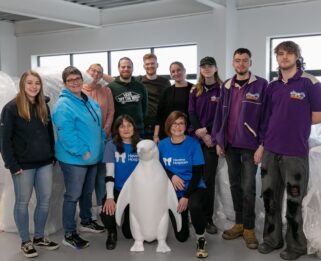 Group of volunteers surrounding a baby penguin penguin sculpture