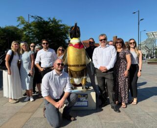 A group of colleagues from Ayers & Cruiks standing around their penguin sculpture which is painted as an emperor.