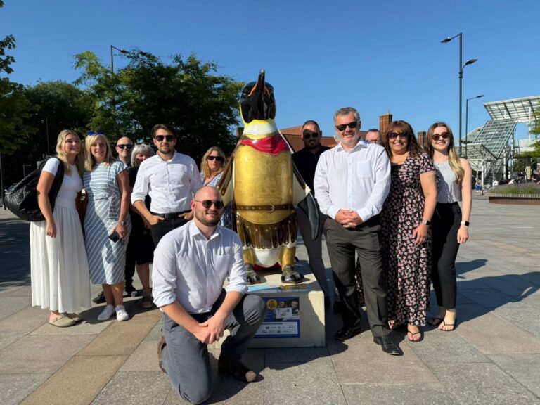 A group of colleagues from Ayers & Cruiks standing around their penguin sculpture which is painted as an emperor.