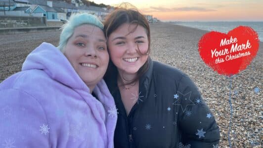 Lucy and Bex to young women smiling at the camera with snowflakes over the top and a heart balloon icon saying make your mark this christmas