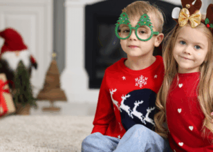 two children wearing festive jumpers and glasses and antlers