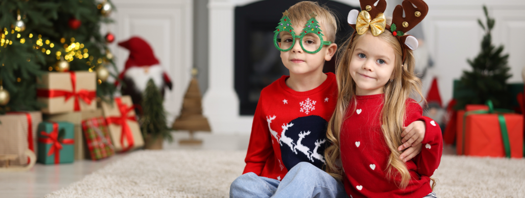 two children wearing festive jumpers and glasses and antlers