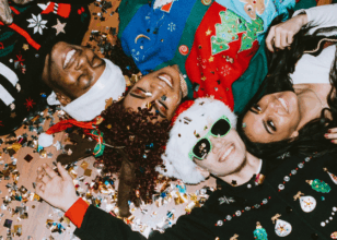 people wearing christmas jumpers smiling laying on the floor looking up at the camera