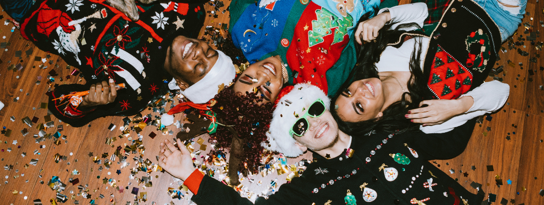 people wearing christmas jumpers smiling laying on the floor looking up at the camera