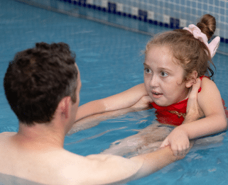 Connie looking at her dad who is holding her in the swimming pool with is outstretched arms