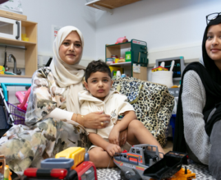 A mother holds her young son as they look at the camera, with a young woman sitting beside them smiling