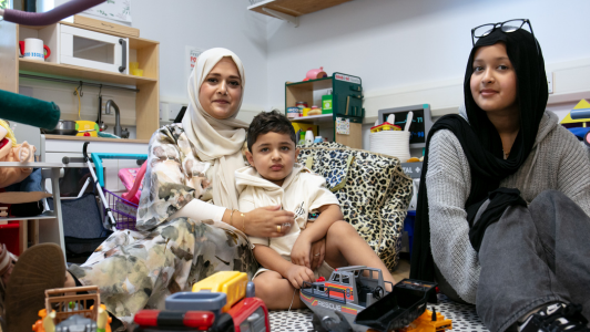 A mother holds her young son as they look at the camera, with a young woman sitting beside them smiling