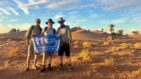 Sahara Trek participants holding havens flag with desert and blue sky behind them
