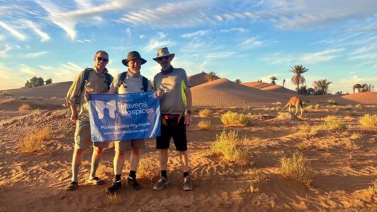 Sahara Trek participants holding havens flag with desert and blue sky behind them