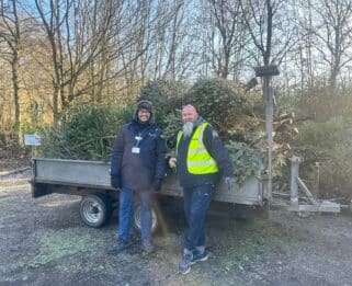 Two men stood in front of a transit van with Christmas trees in the back.
