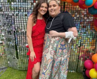 Two women standing in front of a balloon arch smiling.
