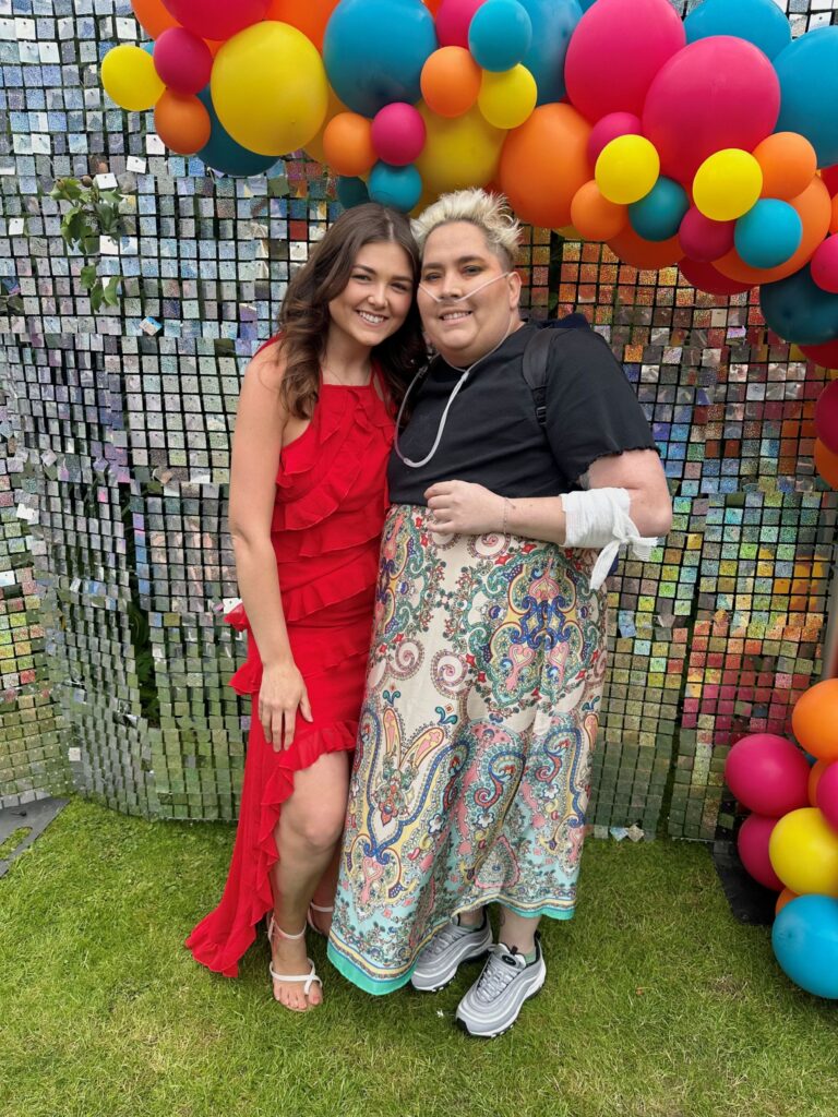 Two women standing in front of a balloon arch smiling.
