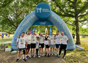 Group of runners in white Utilize tshirts under the blue Havens Hospices running gantry
