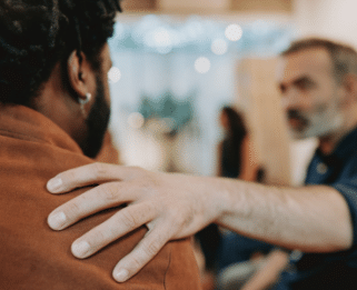 man out of focus with his arm stretch out and his hand on the shoulder of another man who has his back to the camera so you can't see his face