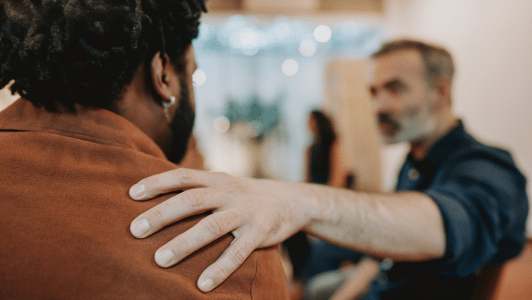 man out of focus with his arm stretch out and his hand on the shoulder of another man who has his back to the camera so you can't see his face