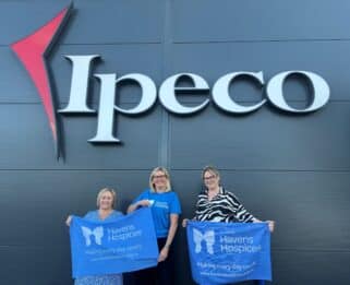 Three women wearing holding Havens Hospices flags outside of IPECO.