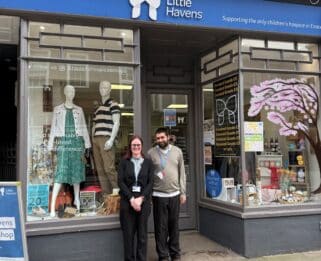 A man and women stood outside smiling in front of a Little Havens charity shop