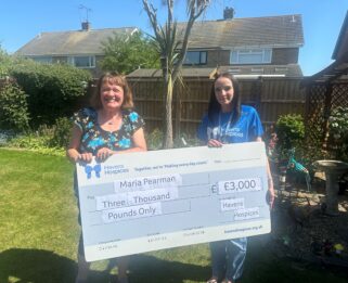 Two women in garden holding a big cheque for £3,000