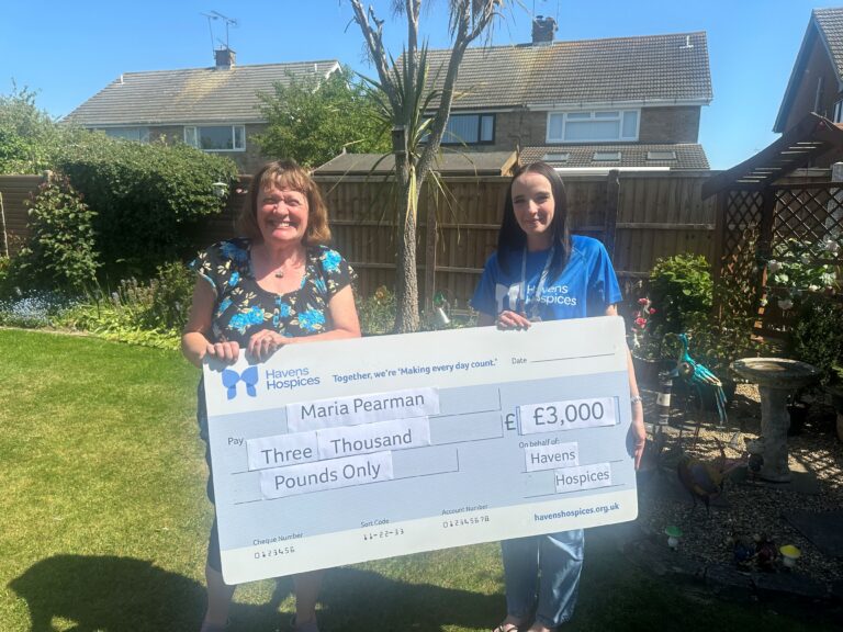 Two women in garden holding a big cheque for £3,000