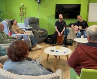 patients sitting down looking at two people singing and playin gthe guitar