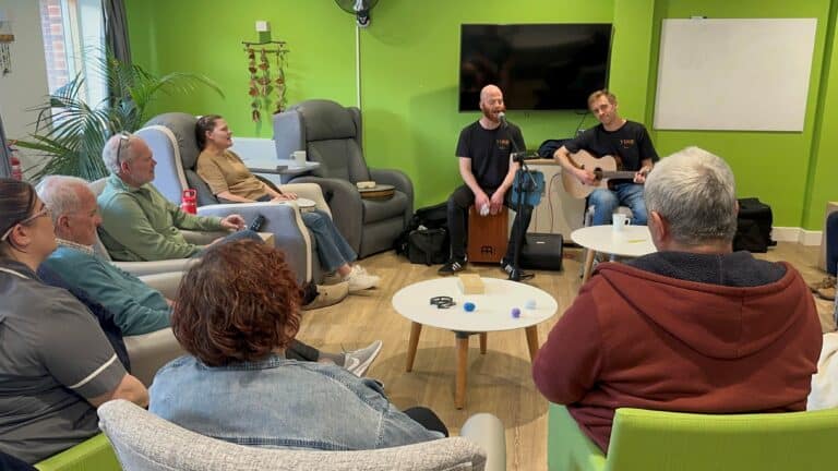 patients sitting down looking at two people singing and playin gthe guitar