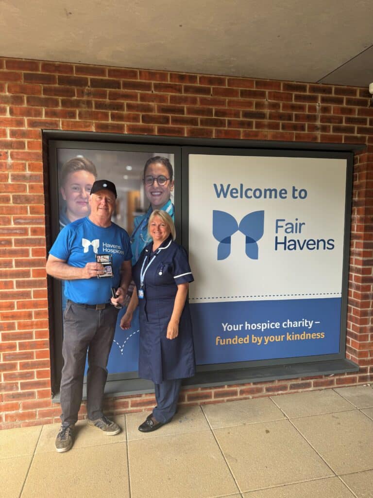 Man in a Havens Hospices top infront of the Fair Havens sign with a nurse.