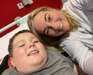 Oliver and his mum Anna laying on a bed smiling at the camera
